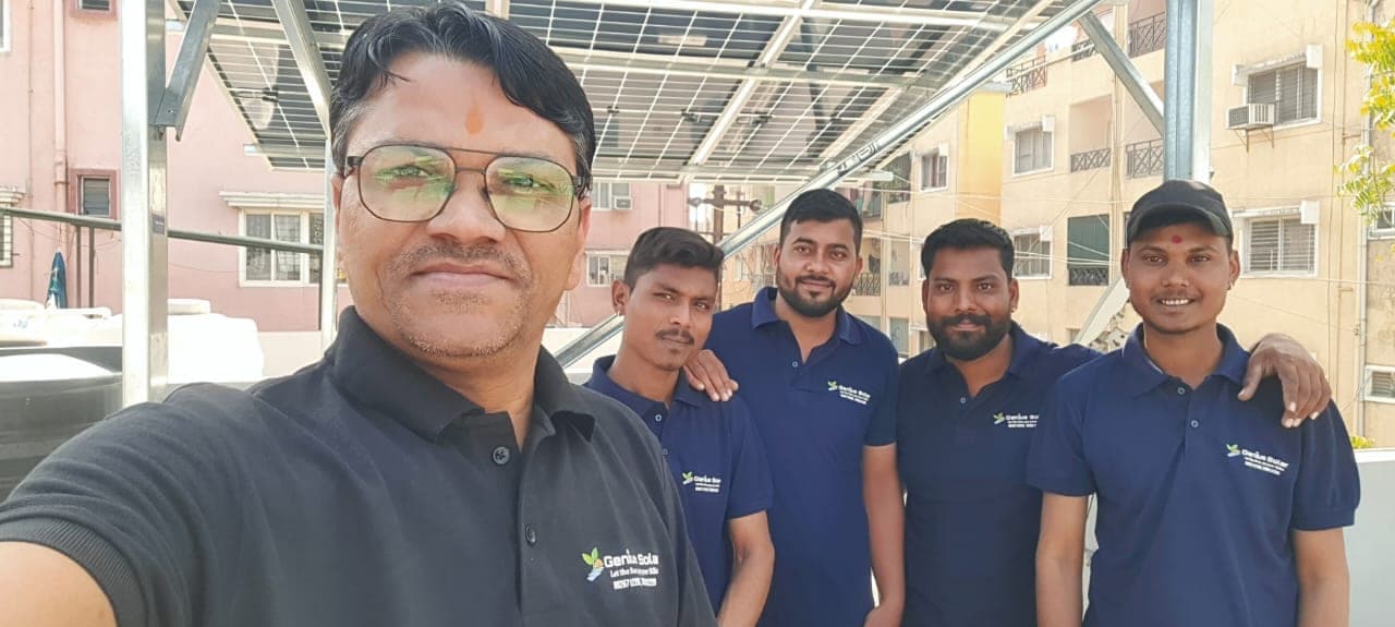 Genius Solar team selfie under a completed elevated solar array in an Indore residential colony