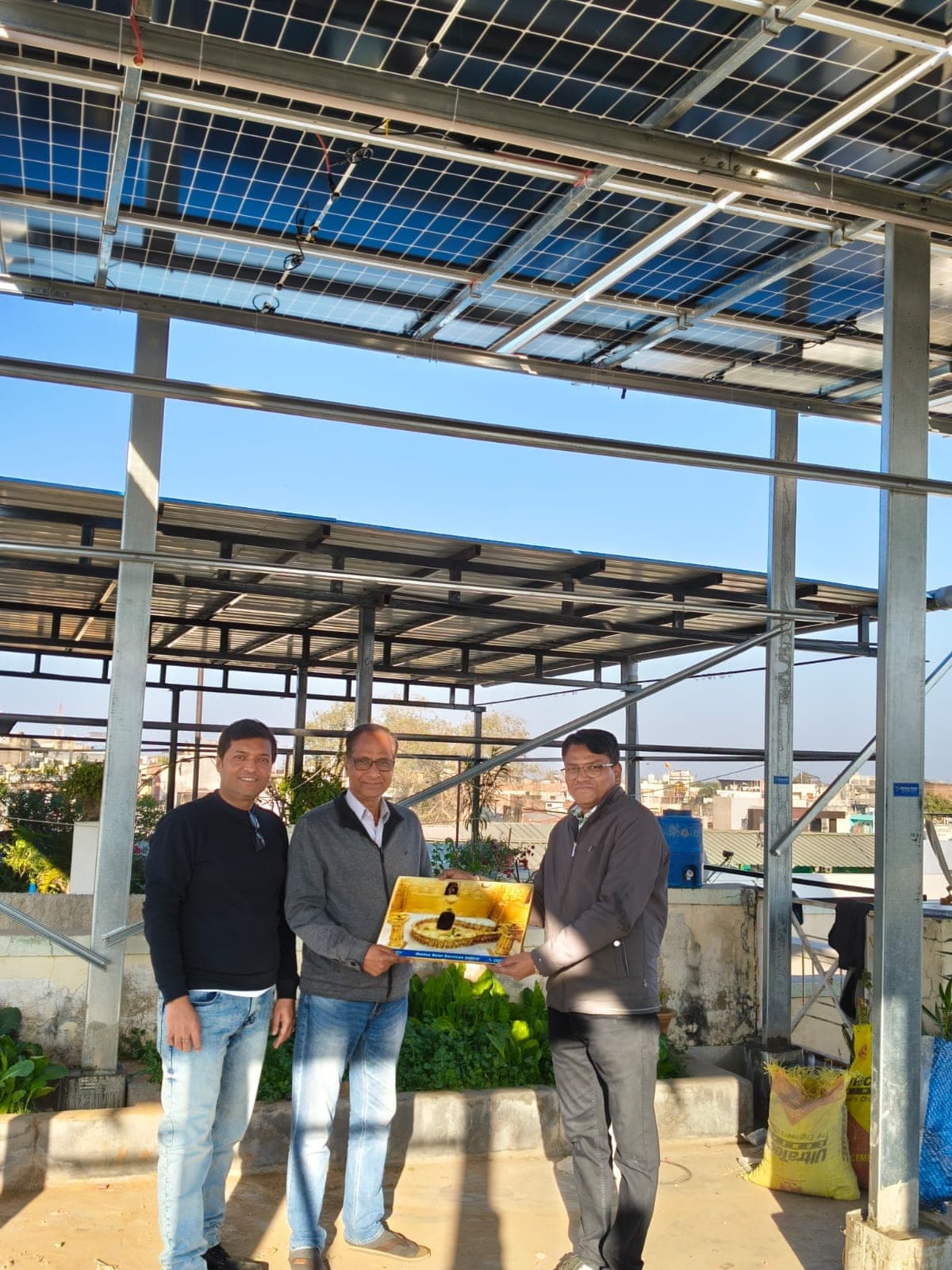 Genius Solar handing over a memento to a customer under a two-level rooftop solar structure in Indore